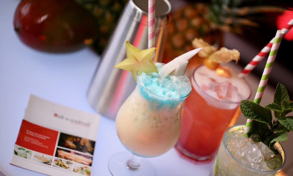 Drei bunte Cocktails auf einer Bartheke mit Call-Cocktails mobile Bar Broschüre
