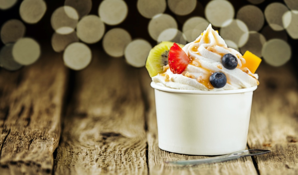 Frozen Joghurt im weissen Pappbecher mit Erdbeeren Kiwi Heidelbeer Topping Firmenevent auf Holzhintergrund