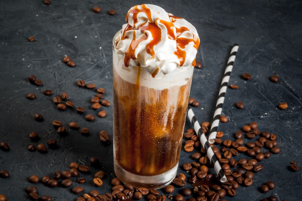 Ice blended Coffee im Glas mit Sahnehaube und Caramel Sirup Papierstrohhalme und Espressobohnen