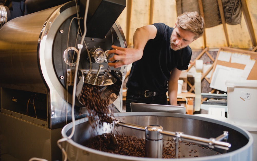 Mann vor Kaffee Röstmaschine lässt geröstete Espressobohnen raus