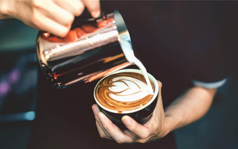 Barista giesst Milch aus Kännchen in Tasse ein Latte Art mobile Erpressobar